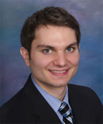 close up headshot of man smiling widely with suit and tie and solid dark blue background