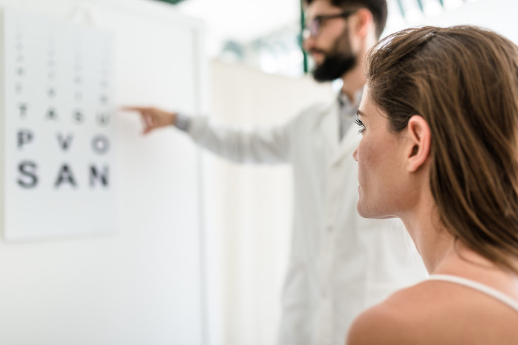 woman staring at vision testing letter sheet on wall as doctor points at it