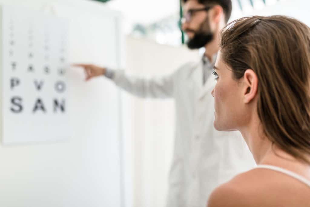 woman staring at vision testing letter sheet on wall as doctor points at it